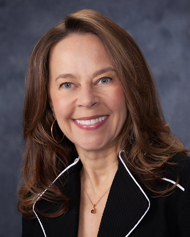 Professional headshot of a woman in a black blazer smiling against a gray background