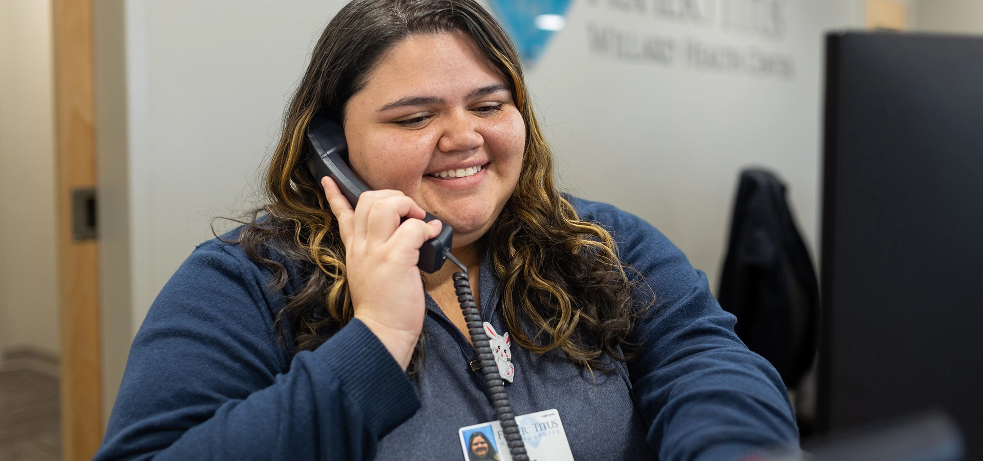 A smiling Fisher-Titus staff member talks on the phone at a reception desk.