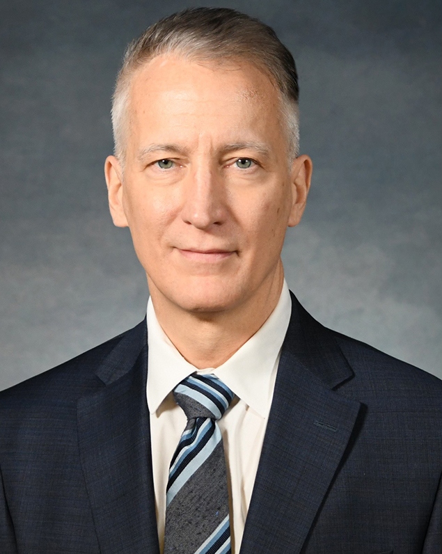 Professional headshot of a man in a navy suit and striped blue tie