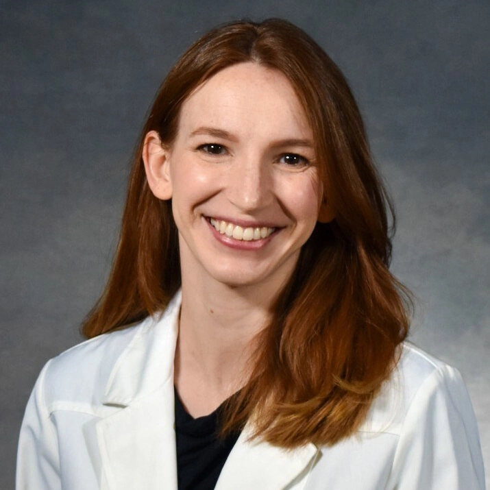 Smiling female physician in a white lab coat against a gray background