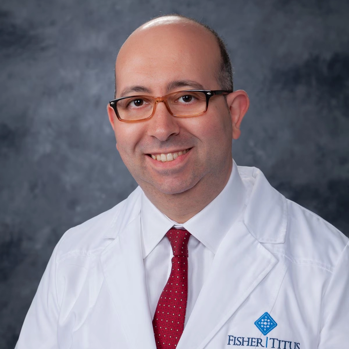 Male Fisher-Titus physician in white lab coat and red tie, smiling in a professional headshot portrait.