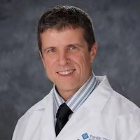 Male healthcare provider in a white Fisher-Titus lab coat smiling professionally